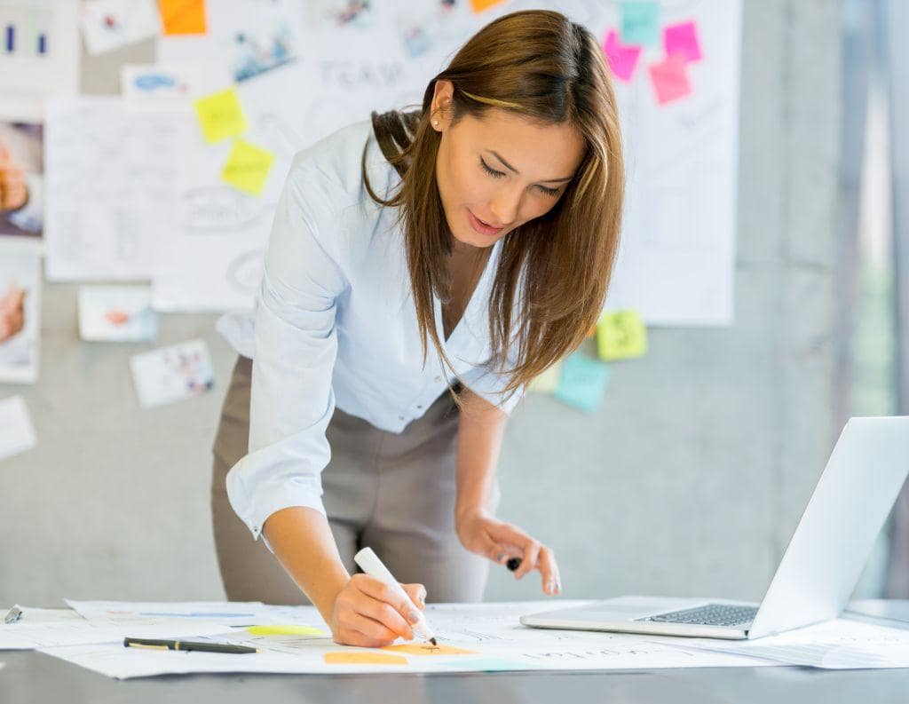 Frau, die Post-Its an einem Tisch beschreibt, mit Metaplanwand im Hintergrund, symbolisiert berufliche Neuorientierung, klare Perspektiven und Work-Life-Balance in einem Workshop-Setting.