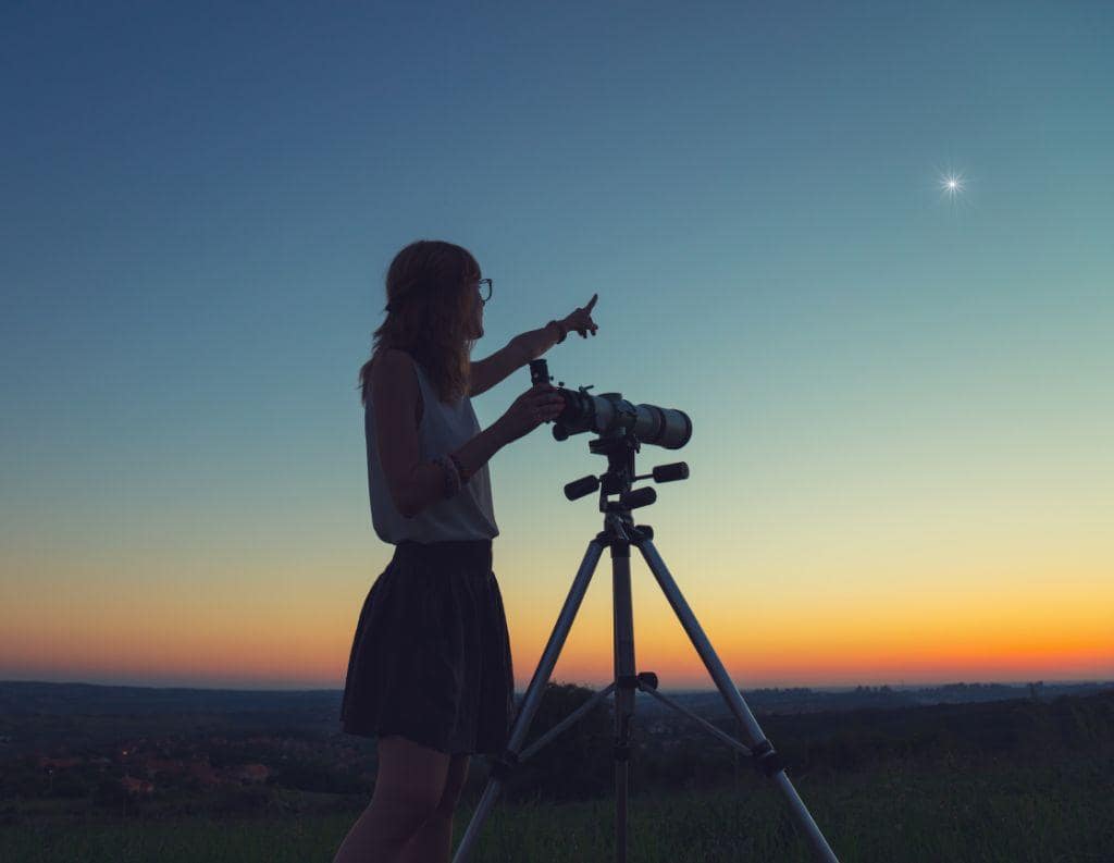 Frau mit Fernrohr, die auf einen Stern am Himmel zeigt, symbolisiert eine neue berufliche Perspektive, klare Ziele und die Verbindung von Zufriedenheit und Work-Life-Balance.