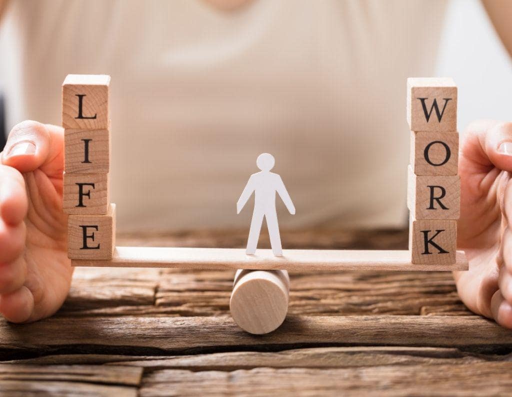 Eine Illustration zeigt eine Wippe, auf der links „Work“ und rechts „Life“ steht – beide Seiten befinden sich im Gleichgewicht, symbolisch für eine ausgewogene Work-Life-Balance.
